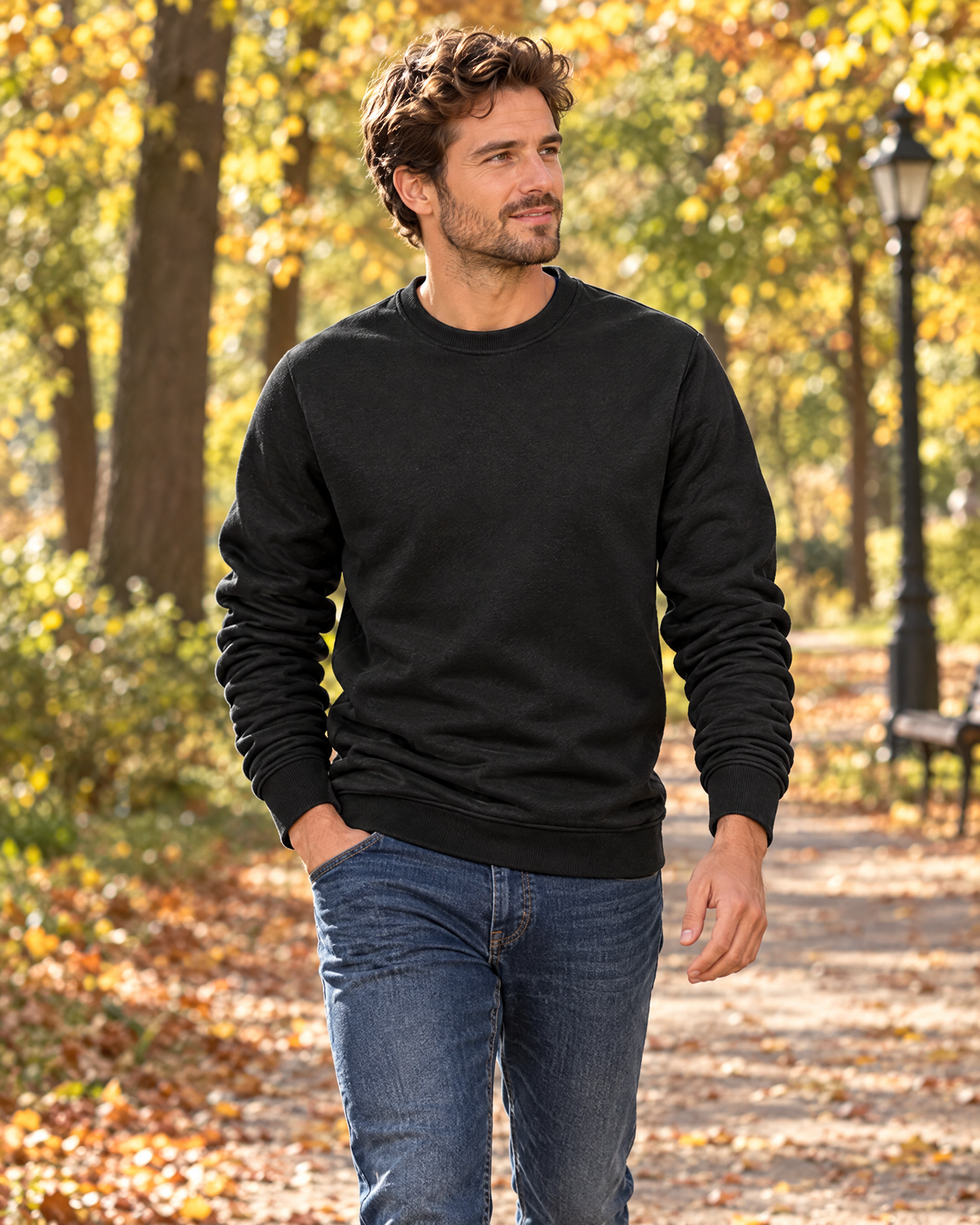 Man walking in a black pullover sweatshirt with jeans on an autumn park path